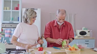 Neşeli son sınıf çifti, taze sebzeleri birlikte hazırlarken, yemek hazırlarken, sevgi dolu anları paylaşıyorlar. Parlak mutfak ortamında.