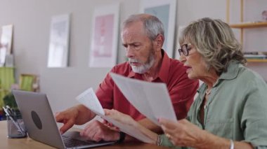Yaşlı çift belgeleri inceliyor ve dizüstü bilgisayar kullanıyor. Yavaş çekimde bilgiyi tartışıyor ve analiz ediyor.