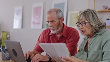 Yaşlı bir çift, ağır çekimde yakalanan dizüstü bilgisayar kullanırken faturalarla ilgili anlaşmazlık yaşıyor.