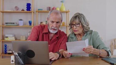 Yaşlı çift dizüstü bilgisayardaki bir belgeyi inceliyor, endişelerini dile getiriyor ve içindekileri yavaş çekimde tartışıyor.