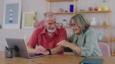 Yaşlı çift birlikte vakit geçiriyorlar, internette dizüstü bilgisayarda geziniyorlar, kahkahaları ve mutluluğu yavaş çekimde paylaşıyorlar.