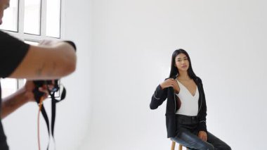 Profesyonel fotoğrafçı, beyaz bir stüdyodaki taburede poz veren bir mankenin resimlerini çekiyor.