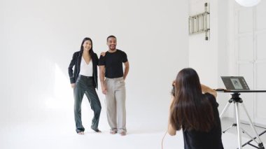 Bir moda fotoğrafçısının beyaz bir arka planda poz veren şık bir çiftin fotoğraflarını çekerken yavaş çekim sahnesi.