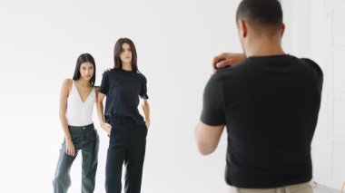 Fotoğrafçı, beyaz arka planda ağır çekimde poz veren iki kadın manken çekiyor.