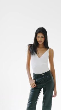 Profesyonel model, gösterişli deri pantolonları ve beyaz bluzuyla ayakta duruyor. Stüdyonun fotoşoplarında el değmemiş beyaz arka plana karşı zarif bir stil sergiliyor.