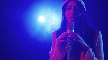 Yetenekli genç bayan şarkıcı sahnede tutkulu bir şekilde şarkı söylüyor, canlı mavi ve kırmızı ışıklarla aydınlatılıyor, yavaş çekimde çekiliyor.