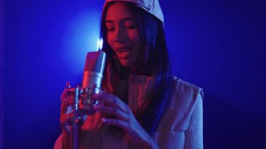 Yetenekli genç bayan şarkıcı, canlı, renkli bir ortamda mikrofonla tutkulu bir şekilde şarkı söylüyor.