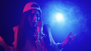 Yetenekli genç bayan şarkıcı tutkulu bir şekilde bir kayıt stüdyosunda şarkı söylüyor, canlı mavi ve kırmızı ışıklarla aydınlatılıyor, büyüleyici bir şekilde yavaş çekimde çekiliyor.