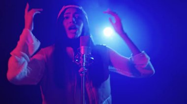 Yetenekli genç bayan şarkıcı, yavaş çekimde çekilen renkli ışıklar altında tutkuyla sahnede şarkı söylüyor.