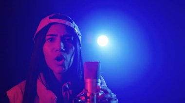 Yetenekli genç bayan şarkıcı sahnede tutkulu bir şekilde şarkı söylüyor, canlı mavi ve kırmızı ışıklarla aydınlatılıyor, yavaş çekimde çekiliyor.