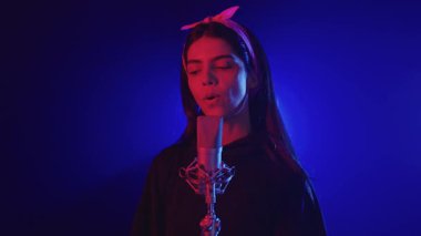 Yüksek enerjili canlı müzik performansı sırasında tutkulu bir şekilde şarkı söyleyen profesyonel kadın vokalist, yavaş çekimde dramatik mavi ve kırmızı sahne ışıklandırmasıyla aydınlatıldı.