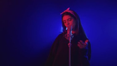 Mavi ve kırmızı sahne ışıkları altında tutkulu bir şekilde şarkı söyleyen genç bir kadının yavaş çekim videosu.