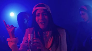 Canlı performans sergileyen genç bir bayan şarkıcının yavaş çekim montajı canlı mavi ve kırmızı ışıklarla aydınlatılıyor.