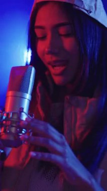 Genç bir kadının tutkulu bir şekilde mikrofona şarkı söylemesi, renkli sahne ışıklarıyla aydınlatılmış, yavaş çekimde.