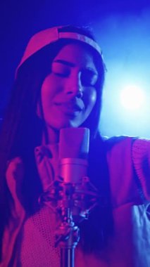 Yetenekli genç bayan şarkıcı, canlı sahne ışıklarıyla aydınlatılmış, mikrofonuyla tutkulu bir şekilde şarkı söylüyor.