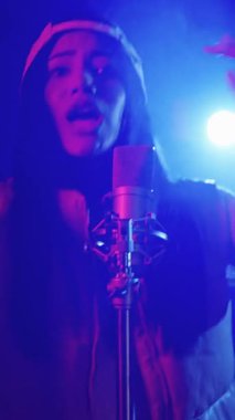 Yetenekli genç bayan şarkıcı sahnede canlı performans sergiliyor, canlı neon ışıklarla aydınlatılıyor, büyüleyici ağır çekimde çekiliyor.