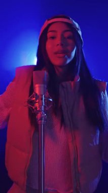 Yavaş çekim, genç bir kadını canlı mavi ve kırmızı sahne ışıklarıyla aydınlatılmış bir mikrofona tutkuyla şarkı söylerken yakalıyor.