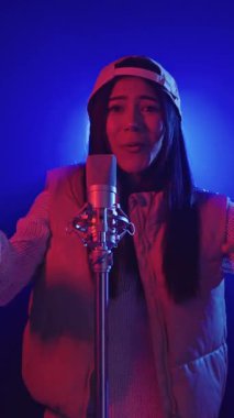 Sahnedeki mikrofona tutkulu bir şekilde şarkı söyleyen genç bir kadının görüntüsü, canlı mavi ve kırmızı ışıklarla aydınlatılmış, yavaş çekimde yakalanmış.