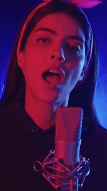 Yetenekli kadın vokalist mikrofona tutkuyla şarkı söylüyor, dramatik mavi ve kırmızı sahne ışıkları altında yoğun duygusal ifadeyle şarkı söylüyor.