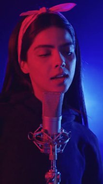 Şarkıcı canlı mavi ve kırmızı ışıklarla aydınlatılmış bir kayıt stüdyosunda tutkuyla şarkı söylüyor.