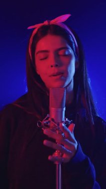 Yavaş çekim, canlı mavi ve kırmızı sahne ışıklarıyla aydınlatılmış yoğun duygularla şarkı söyleyen genç bir kadını yakalıyor.