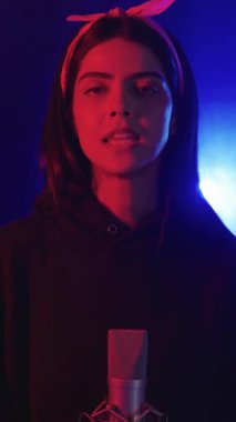 Genç bir kadın yoğun duygularla şarkı söylüyor, canlı, renkli sahne ışıkları tarafından yavaş çekimde aydınlatılıyor.