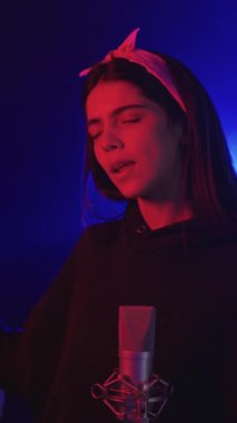 Sahnede canlı performans sergileyen genç bir kadın şarkıcının montajı. Mavi ve kırmızı ışıklarla aydınlatılmış, ağır çekimde şarkı söyleyen.