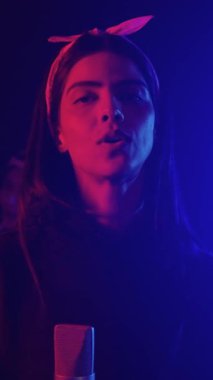 Kadın vokalist, loş bir sahnede tutkulu bir canlı müzik icra ediyor, canlı renkli ışıklar yavaş çekimde duygusal müzik anını vurguluyor.