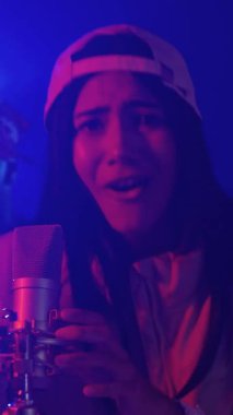 Tutkulu genç vokalist mikrofona yoğun bir şekilde şarkı söylüyor, etkileyici enerji ve müzikal duygularla ağır çekimde dramatik bir şekilde çekiliyor.