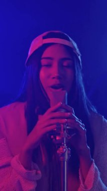 Enerjik genç bayan şarkıcı canlı, neon ışıklı bir ortamda tutkulu bir performans sergiliyor.