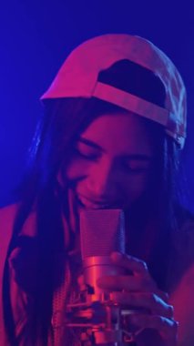 Beyzbol şapkası takan genç bayan şarkıcı canlı ve renkli bir sahnede tutkulu bir şekilde mikrofona şarkı söylüyor.