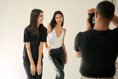 Fotoğrafçı, beyaz arkaplan ile profesyonel bir stüdyoda poz veren iki gülümseyen mankenin fotoğraflarını çekiyor.