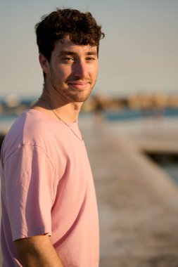 Sahil kenarında altın saatin tadını çıkarırken huzur içinde gülümseyen genç bir adamın portresi.