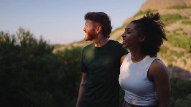 Manzaralı dağ manzarasında yürüyüş yapan, neşeli anları paylaşan ve yaz macerasında doğal güzellikleri keşfeden çok kültürlü bir çift.