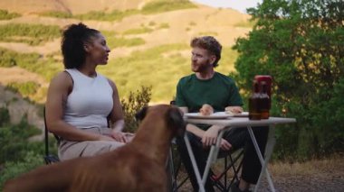 Milenyum çifti evcil boksörle rahatlıyor, dağ minibüsünün yanında yemek ve bira paylaşıyor, altın saat günbatımında kaygısız yolculuk yaşam tarzını somutlaştırıyor.