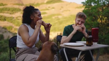 Minibüs macerası sırasında dışarıda yemek yerken köpekleriyle sosisli paylaşan çok ırklı mutlu çift.