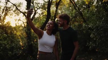 Günbatımında ormanda selfie çeken çok ırklı genç bir çift minibüs maceralarının tadını çıkarıyorlar.