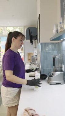 Professional female worker with black gloves pouring apple juice from a carton into a blender, preparing a healthy smoothie in a cafe