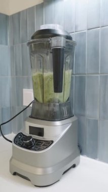 Modern electric blender mixing a fresh green smoothie in slow motion. Healthy breakfast preparation on a kitchen countertop
