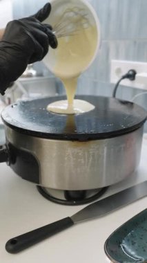 Professional chef in black gloves pouring fresh batter onto a hot electric crepe maker. Slow motion footage showing the process of cooking pancakes