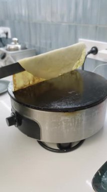 Professional chef in black gloves using a spatula to skillfully flip a thin, delicate crepe on an electric griddle in a kitchen