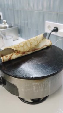 Slow motion shot of a cook in black gloves folding a freshly made pancake with chocolate filling using a spatula on a hot electric griddle