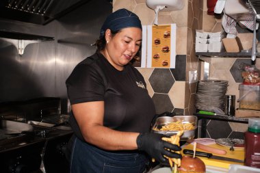 Chef assembling a fresh burger and golden french fries in a professional kitchen, preparing fast food for customers
