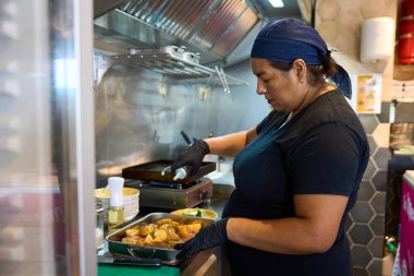 Woman chef in uniform and gloves preparing food on the grill, working hard in a professional restaurant kitchen