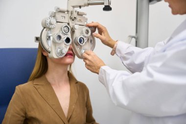 Optometrist adjusting phoropter for a woman undergoing a vision exam in a clinic, focusing on eye healthcare