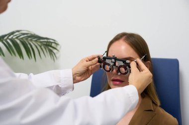 Healthcare professional performing a vision test on a woman using an optical trial frame in a modern optometry clinic