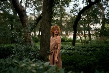 Woman with vitiligo and curly hair standing thoughtfully in a forest, embracing her unique skin condition