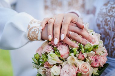 Nikah buketinde alyansları olan yeni evlilerin elleri. Gelinin ve damadın elleri bir buket çiçekte.