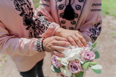 Nikah buketinde alyansları olan yeni evlilerin elleri. Gelinin ve damadın elleri bir buket çiçekte.