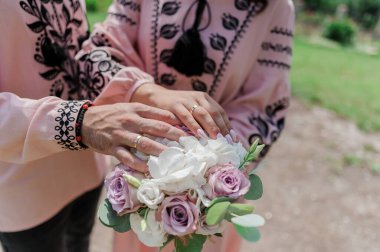 Nikah buketinde alyansları olan yeni evlilerin elleri. Gelinin ve damadın elleri bir buket çiçekte.